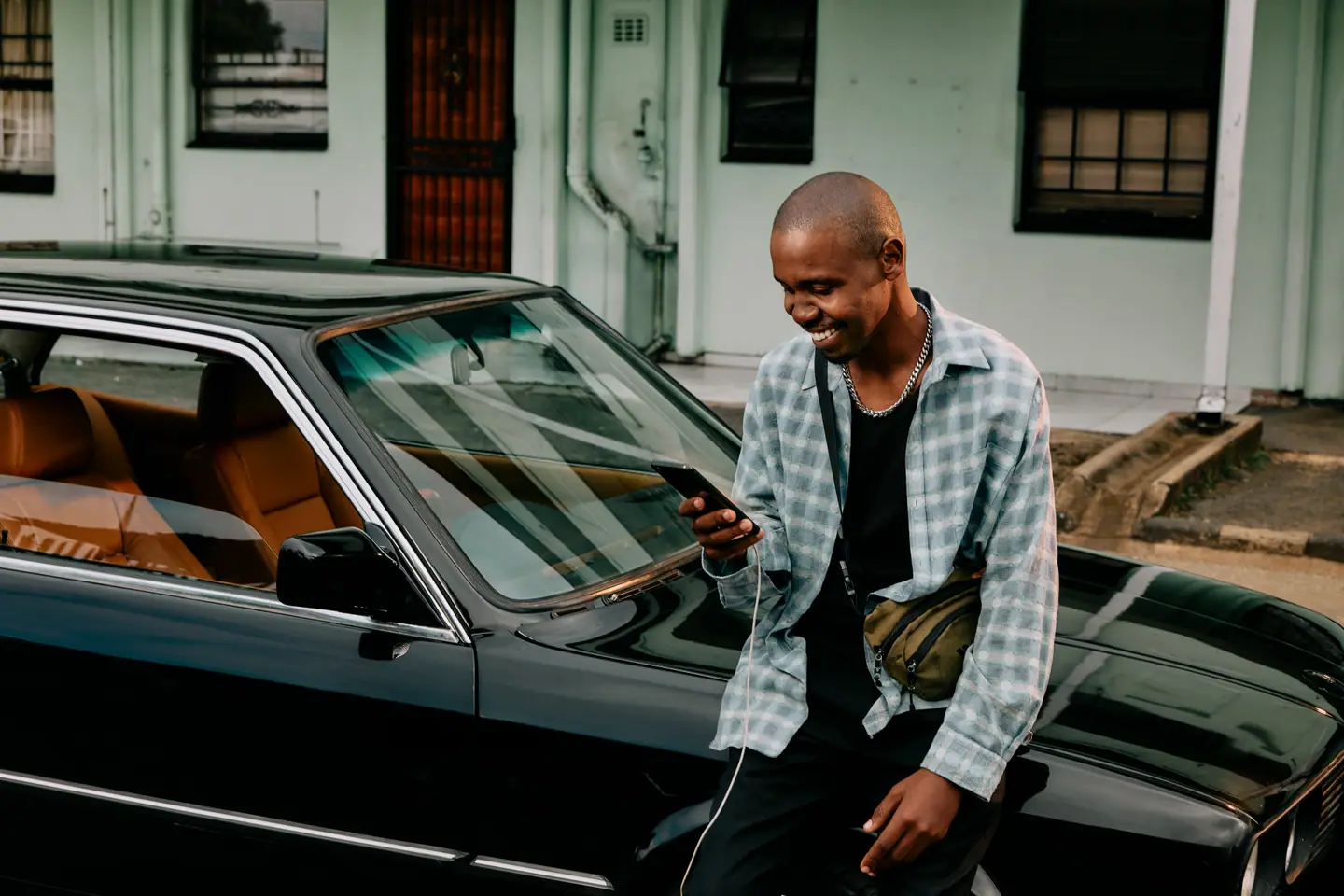 A bPOWERd customer smiling at his phone, leaning on his car